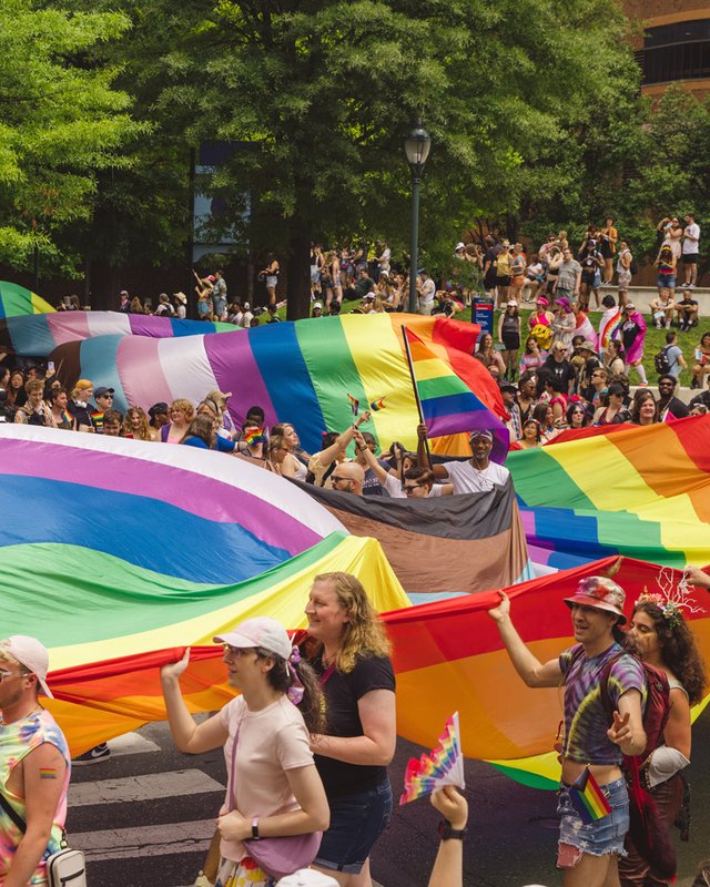 Marchers in a crowded street holding a large rainbow flag at the Philly Pride event