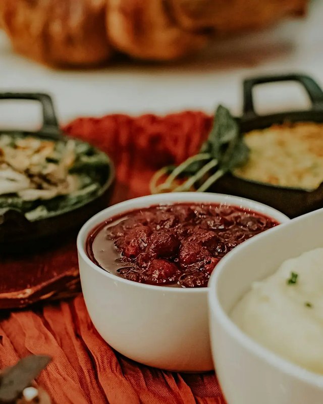 Holiday buffet spread of mashed potatoes, casserole and cranberry sauce in bowls on a rust-colored cloth