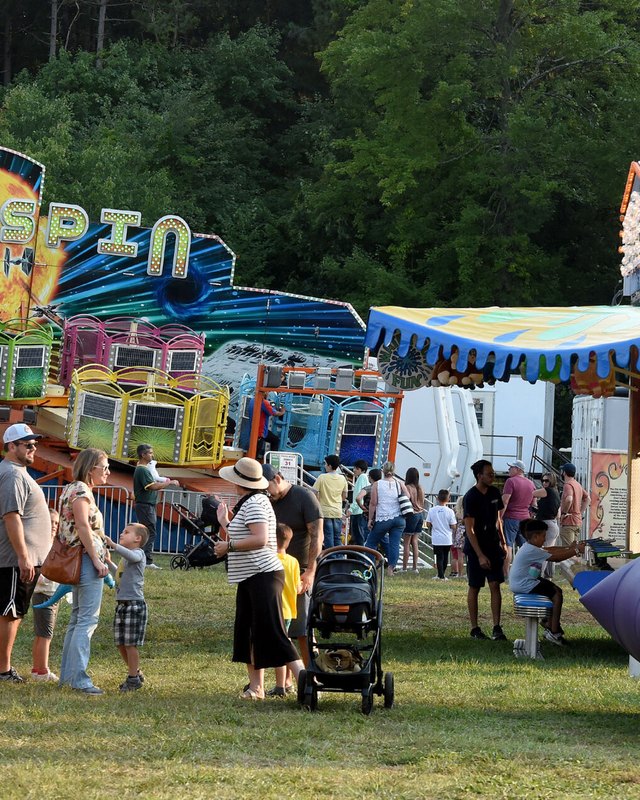 Crowd of visitors walking past a colorful Hyperspin ride and booths on the midway at the Wapping Fair