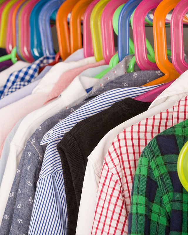 Assorted shirts and clothing on colorful plastic hangers on a clothing rack