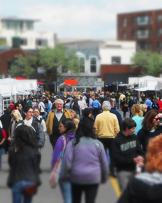 Crowd of shoppers walking past white booth tents at an outdoor street market