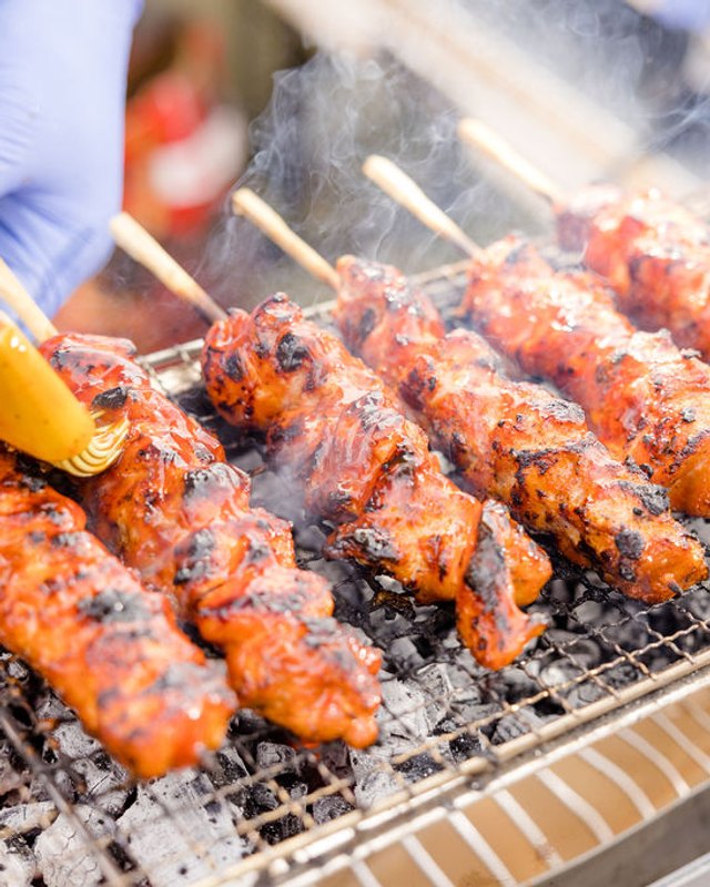 Chicken skewers grilling over charcoal at a food booth at the festival