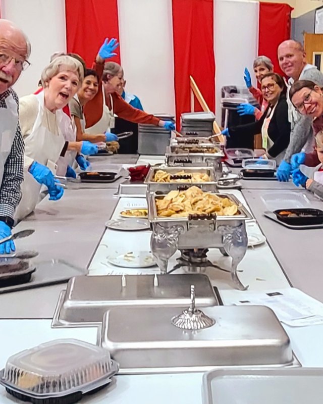 Volunteers in blue gloves serving food from steam trays along a buffet table at a Polish festival kitchen