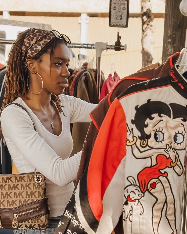 Shopper sorting vintage clothing on a rack at an outdoor market stall.