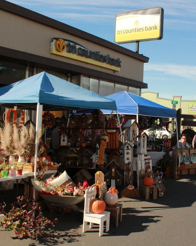 Market booths with blue canopy tents and displayed goods on a street with shoppers nearby