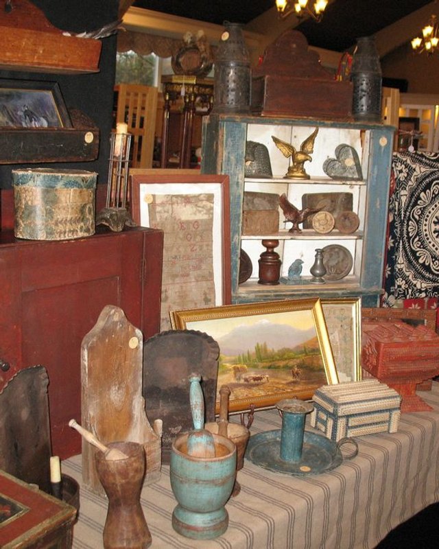 Antiques and collectibles on display, including wooden boxes, lanterns, carvings and framed pictures on a draped table.