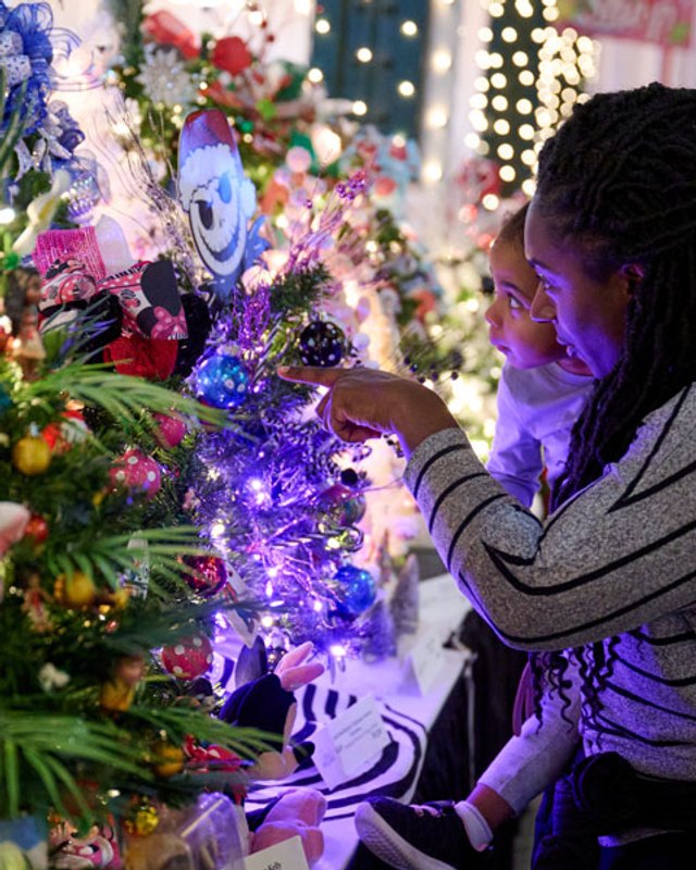 A woman decorating a brightly lit tree with ornaments at a holiday display.