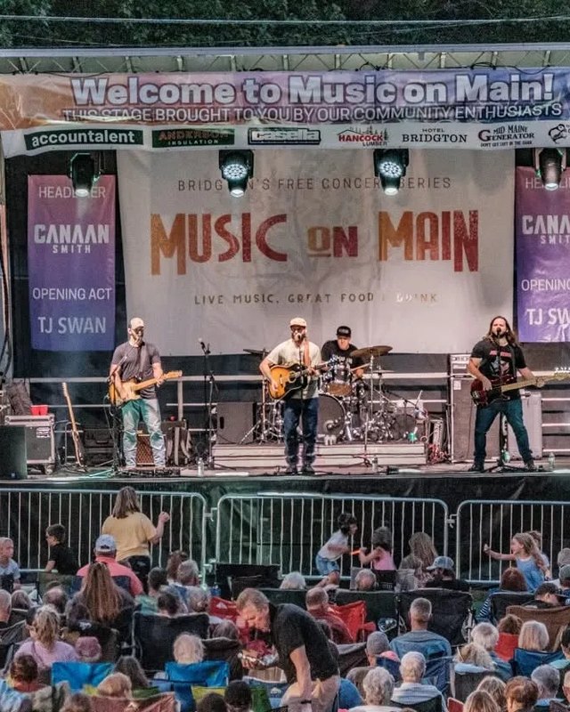 Band performing on the Music on Main stage in front of a crowd of listeners at an outdoor evening concert.