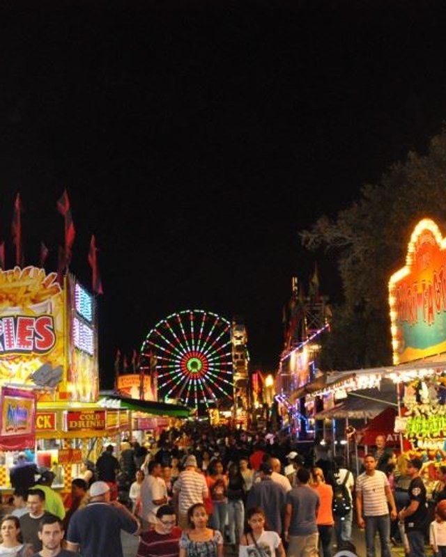 Crowd walking past carnival food booths and rides at night at the Osceola County Fair