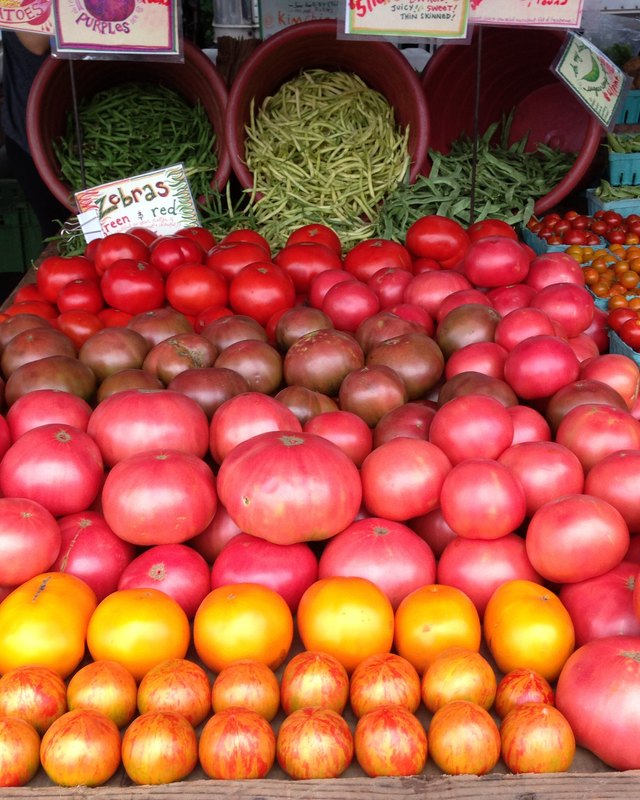 Display of red, pink and yellow tomatoes and green beans in baskets at a produce stand