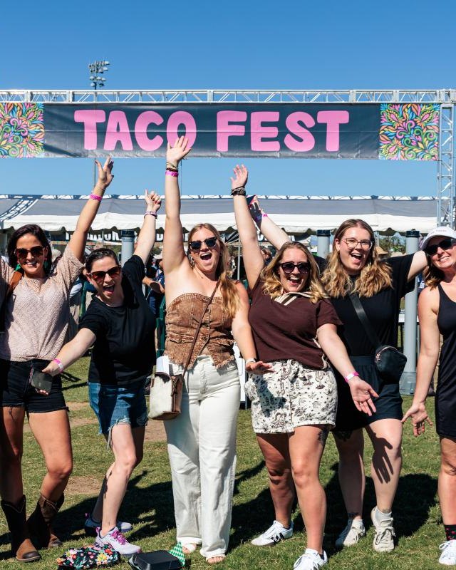 Group of friends cheering with arms raised under the TACO FEST sign at Salt River Fields