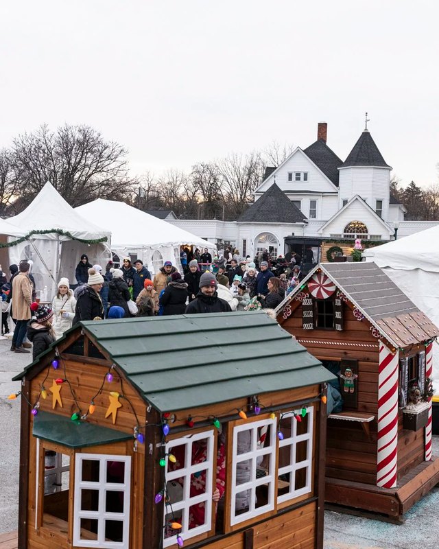 Market tents and wooden holiday village houses with a crowd of shoppers at the Kris Kringle Market in Rochester.