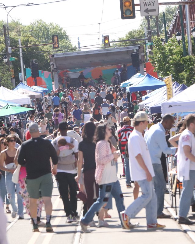 Crowd of shoppers walking past white vendor tents along a Girard Avenue street fair.
