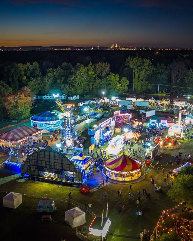 Aerial night view of the festival grounds with lit rides and tents among trees