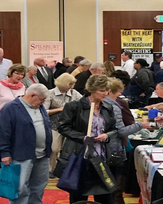 Older shoppers browsing booths at an indoor trade show hall