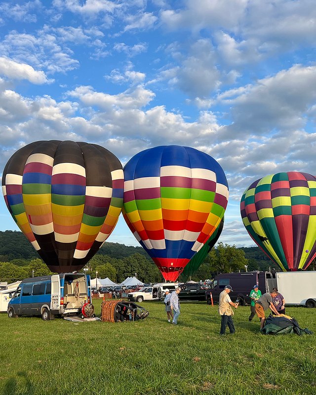 Hot air balloons being inflated on a grass field with people and vehicles nearby under a blue sky