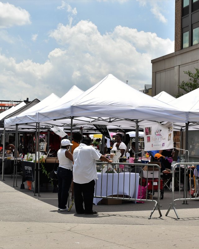 White market tents with shoppers and vendors along a street at an outdoor flea market.