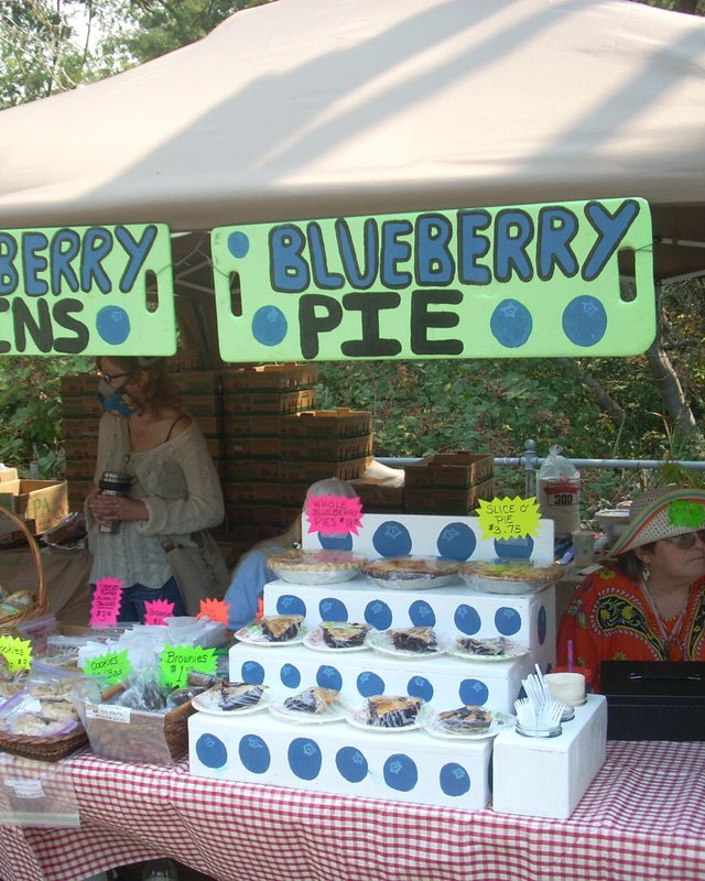Blueberry muffin and blueberry pie booth under a tent, with people behind the table