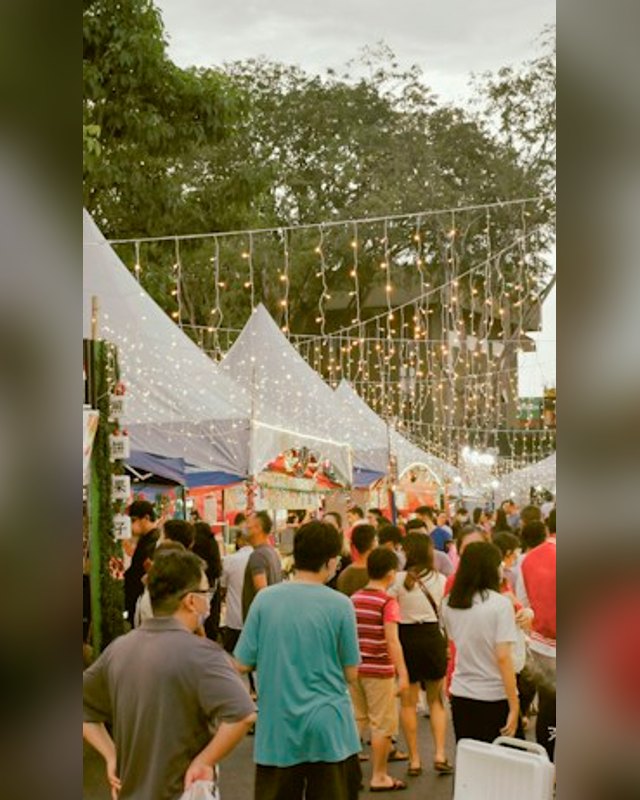 Crowd browsing a lively outdoor market with white tents and string lights overhead
