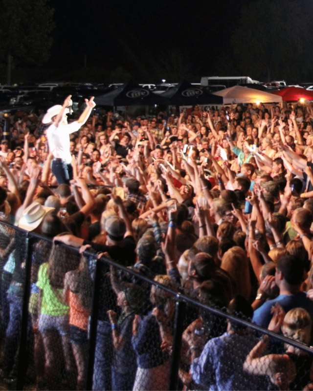 Large crowd of fairgoers packed in front of a stage at night, with a performer above them.