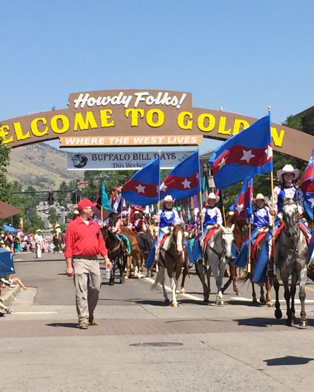 Parade riders with flags passing under the Welcome to Golden arch on a Golden street