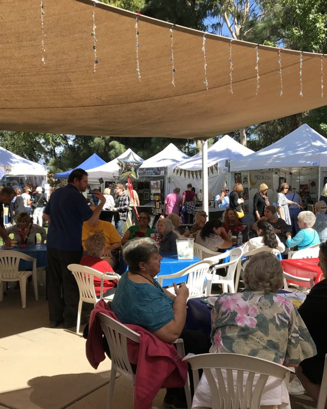 Crowd of visitors seated and browsing under white tents at an outdoor art festival.