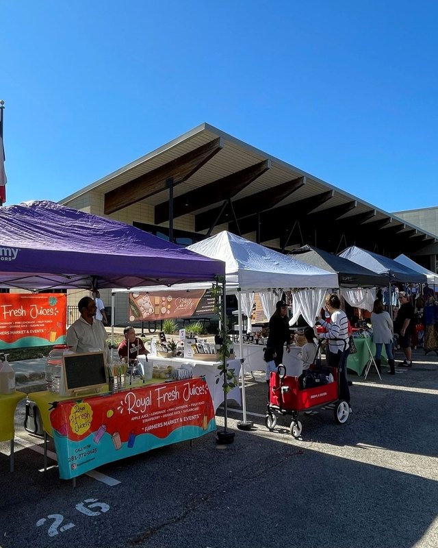 Market vendor tents and booths lining a path at the Imperial Park farmers market in Sugar Land