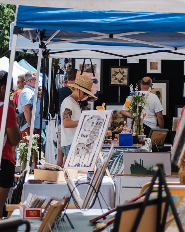 Shoppers browsing artist booths with blue canopies at the Art for the Cash Poor fair in Philadelphia