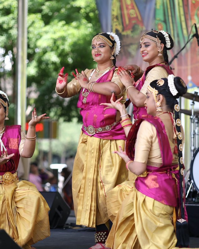 Festival of Joy dancers in pink and gold costumes performing on a stage at Klyde Warren Park