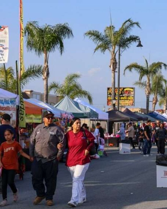 Shoppers walking past vendor tents and white canopies on a palm-lined street at the South El Monte Night Market.