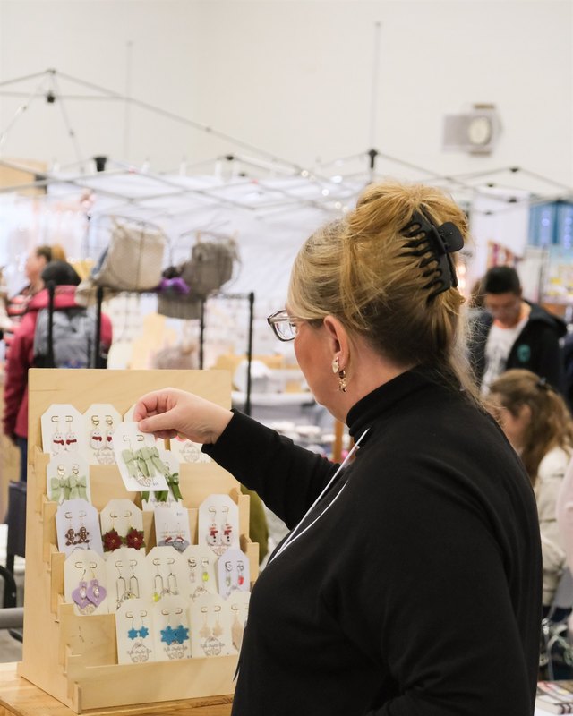Vendor at a craft booth with handmade cards on display, with shoppers in the background at an indoor market.