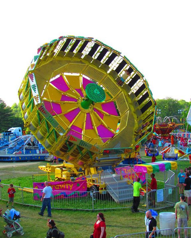 Colorful spinning ride and crowds of visitors on the grass at a Ballwin Days festival midway.