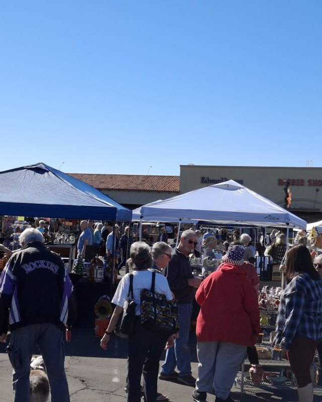 Shoppers browsing under blue and white vendor tents at the Sundome Plaza arts and crafts show in a sunny parking lot.