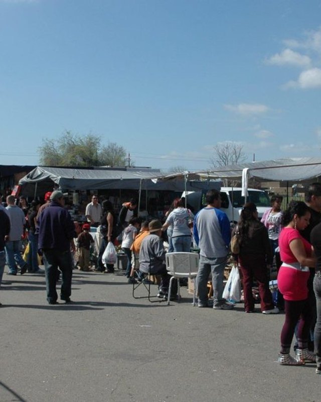 Crowd of shoppers walking among market stalls and food vendors at an outdoor flea market.
