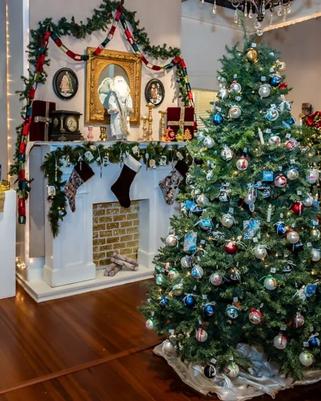 Holiday tree with blue and silver ornaments and garland beside a decorated white mantel at LeMoyne Arts.