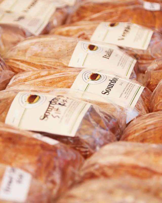 Loaves of bread in clear plastic bags with handwritten or printed labels, such as Sourdough, displayed for sale at the Downtown Rochester farmers market.