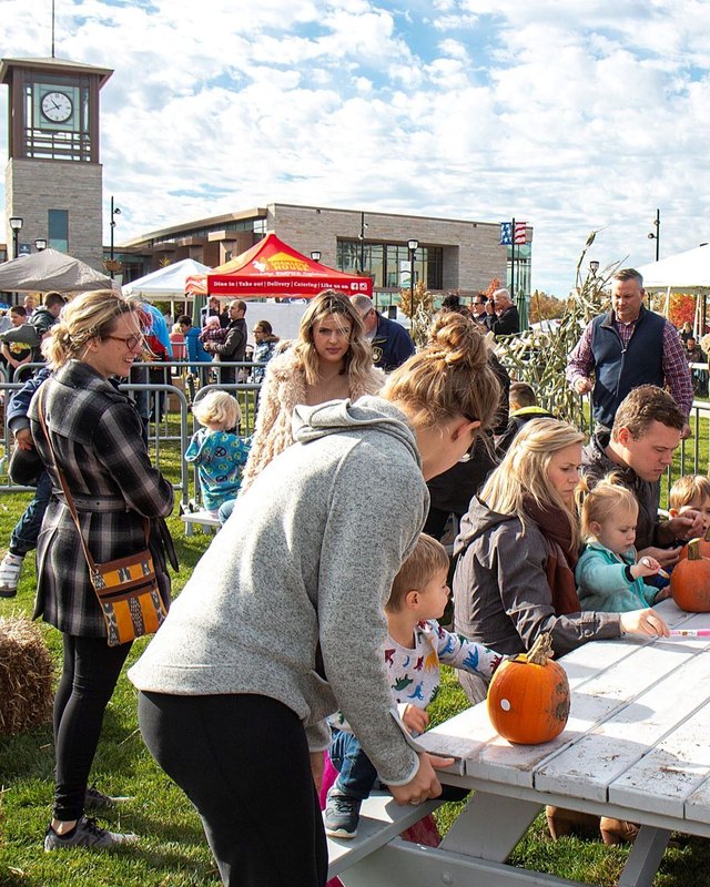 Families decorate pumpkins at tables among booths at the Oak Creek Fall Festival