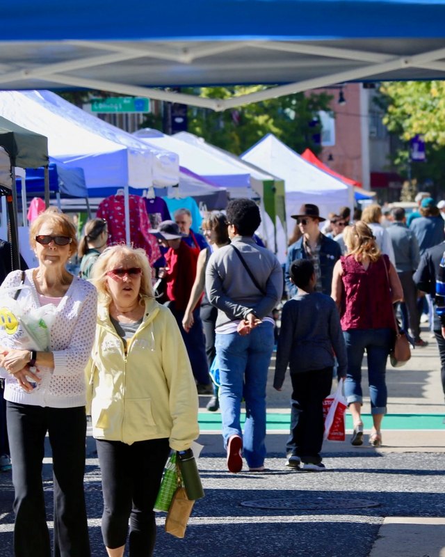 Shoppers walking past market tents on a sunny street during the Collingswood Book Festival