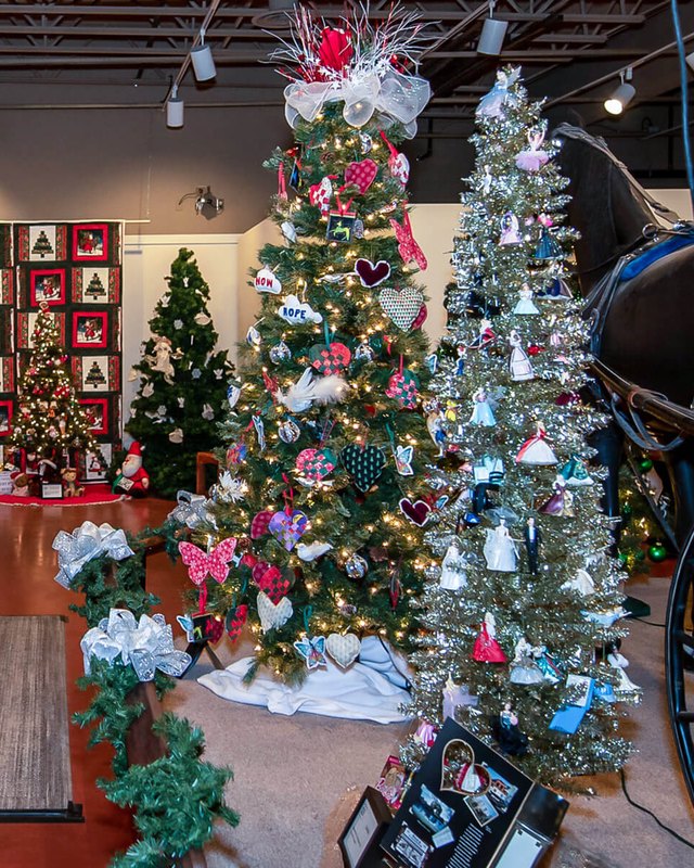 Decorated Christmas trees and a horse-drawn carriage on display in a museum room.