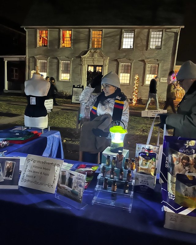 Vendor tables with holiday goods set up outside a lit historic house at night