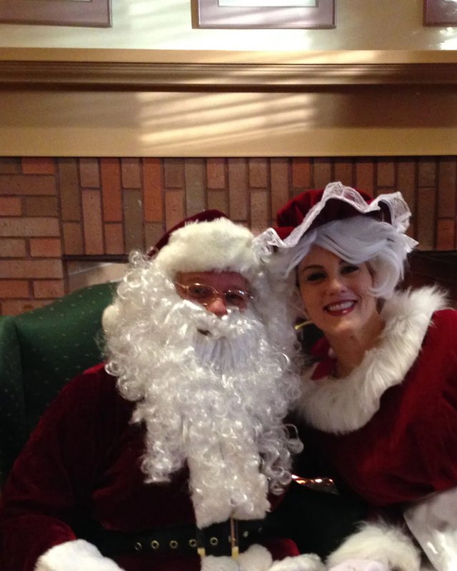 Santa and Mrs. Claus seated by a brick fireplace at the Madeleine Marketplace