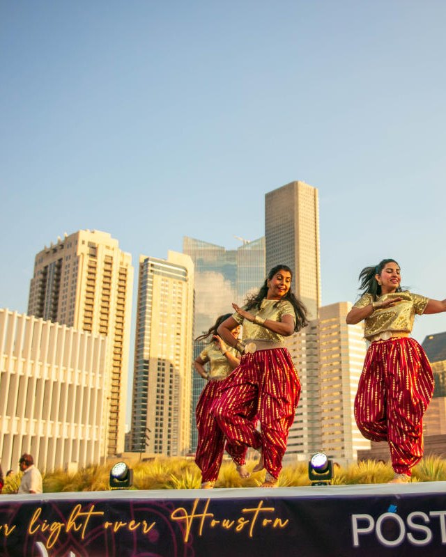 Dancers in traditional dress performing on a stage in front of the Houston skyline at HTX Diwali