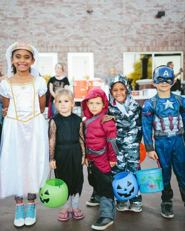 Children in Halloween costumes posing together at an outdoor Tricks & Treats event.