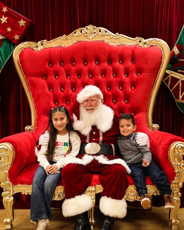 Santa seated in a red throne with two children beside him at the Historic Mission Inn Festival of Lights.