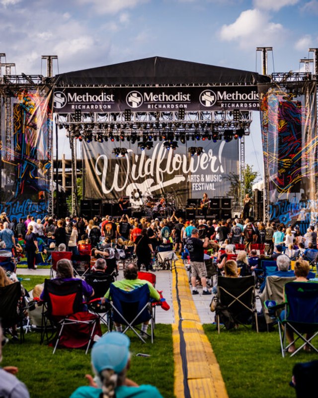 Crowd seated on lawn facing the Wildflower stage with Methodist banners at a Richardson festival, daytime.