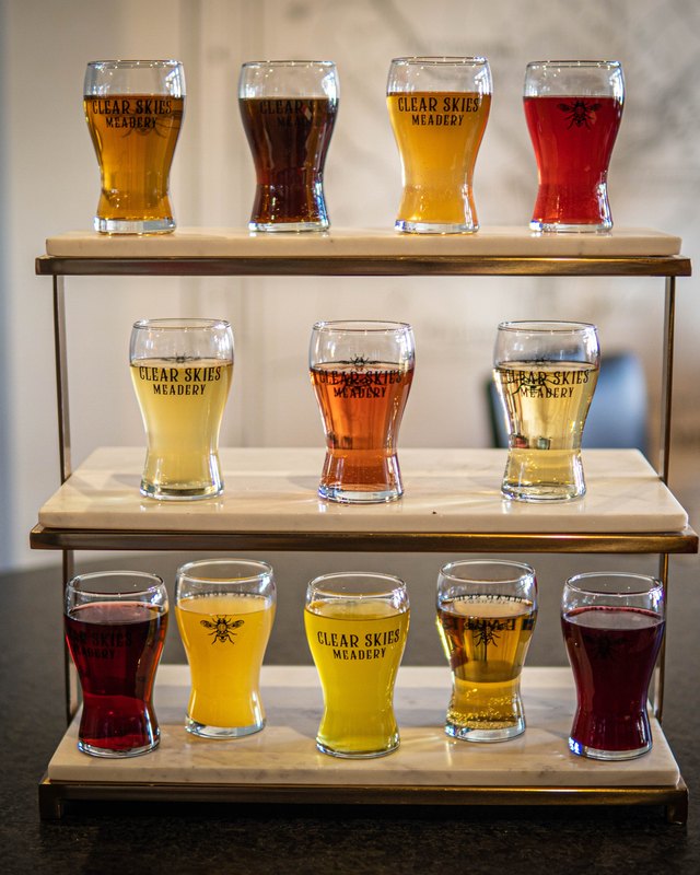 Flight trays of Clear Skies mead samples in branded glasses, shown on wooden racks.