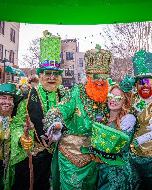 Costumed green-clad parade participants posing together on a downtown street during the St. Patrick's Day parade.