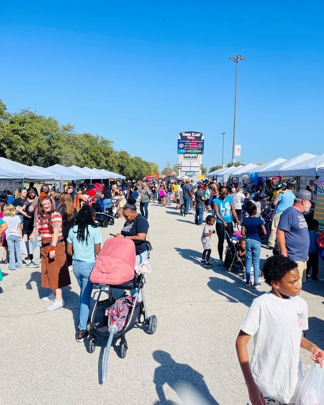 Kids and families walking through the crowded Read Play Talk Festival lot with tents in the background.