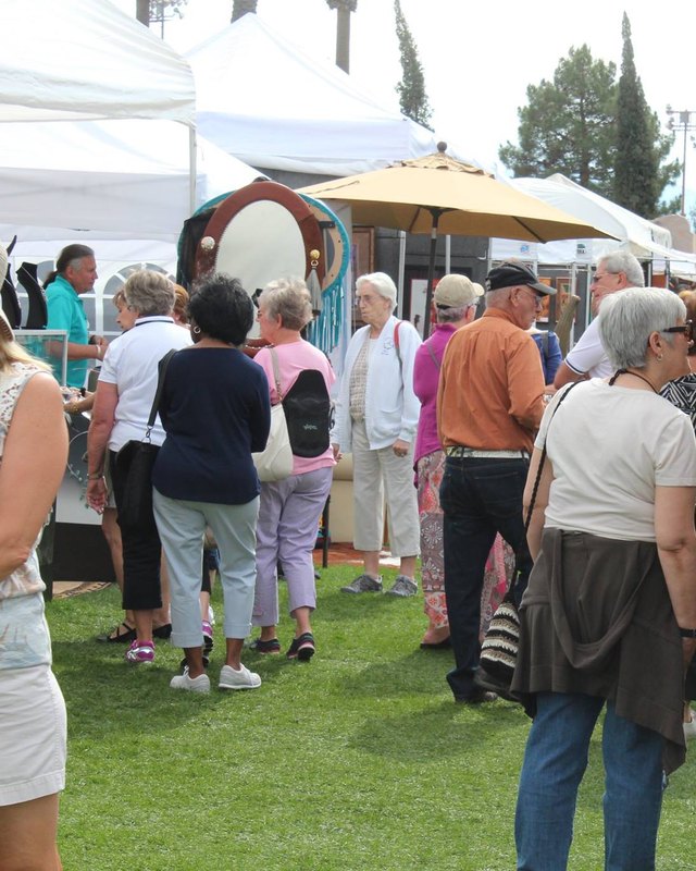 Shoppers and visitors walking past white tent booths on a grass lawn at a festival