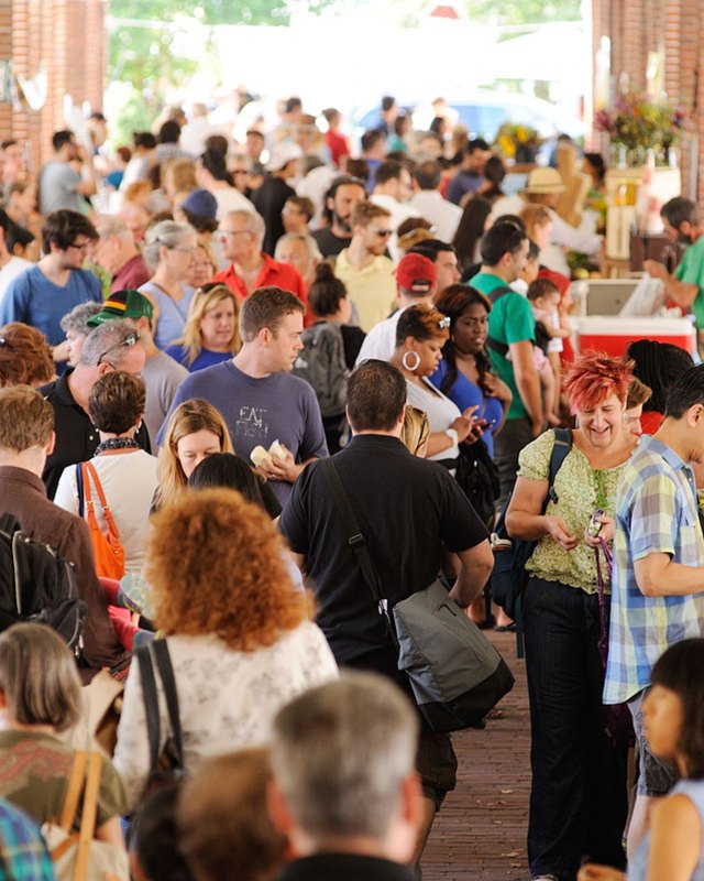 Dense crowd of shoppers browsing produce stands at the Headhouse Farmers Market under a brick arcade.